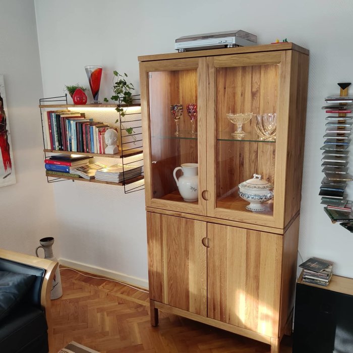Ett handgjort vitrinskåp i massiv ek med glasdörrar, bredvid en stringhylla med böcker och dekor följt av en CD-samling.