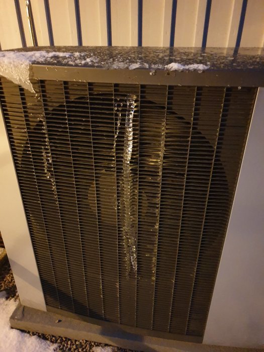 Luftvärmepump med isbildning och snörester på utsidan under vintern.