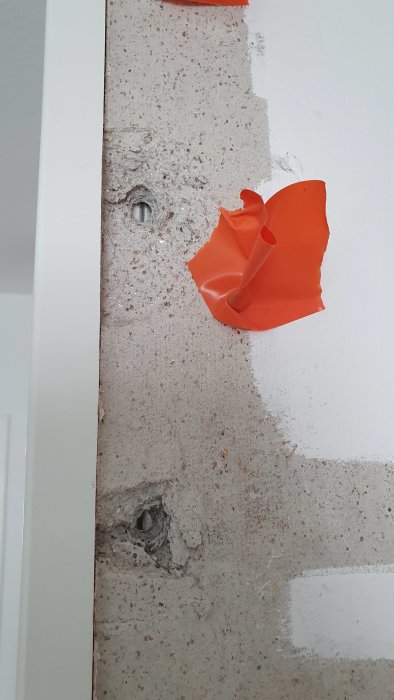 Vägg med glittrande material från 60-talet med borrade hål och en orange plastbit som täcker delar av bilden.