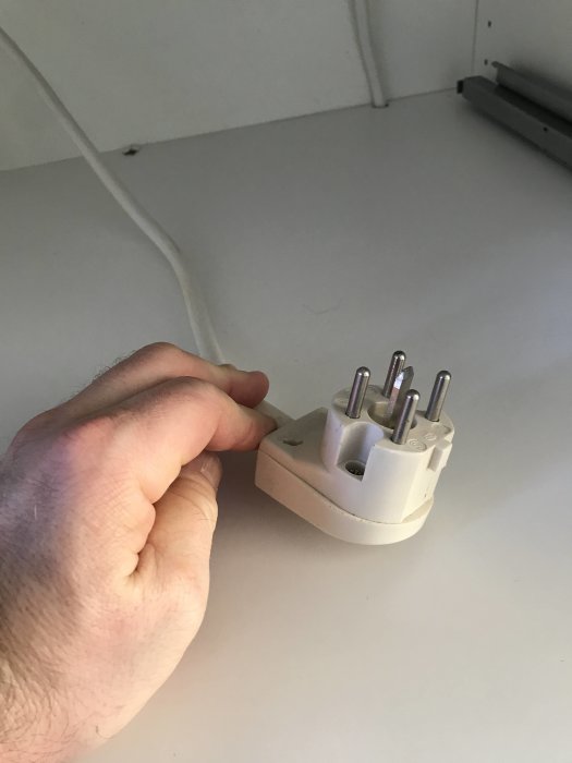 Hand håller en Perilex stickkontakt med fem poler kopplad till en vit kabel mot en köksbänk.