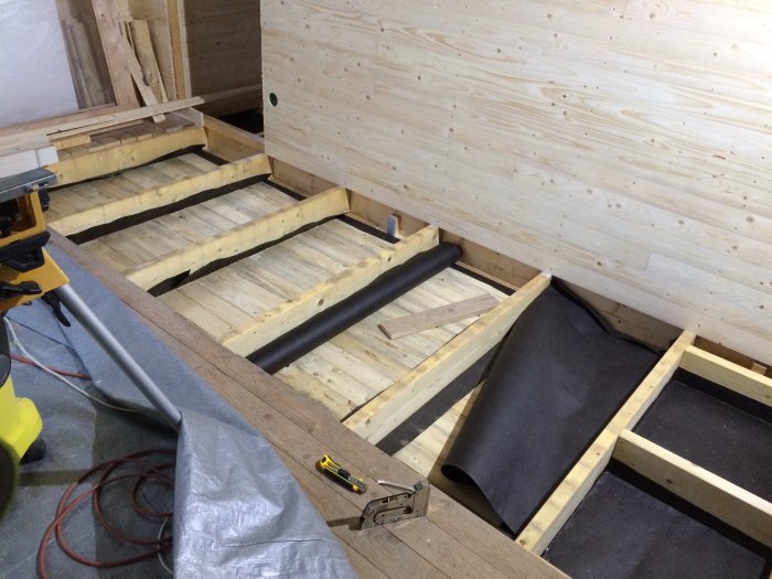 Golvbjälklag under isolering med synliga träreglar och isoleringsmaterial i pågående arbete.