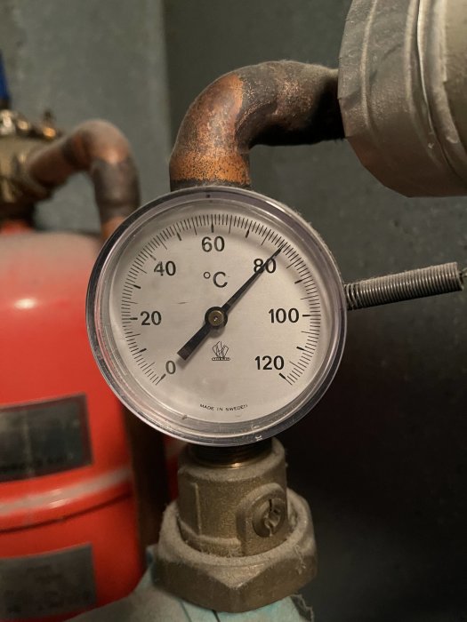 Temperaturmätare på vattenrör visande cirka 60 grader Celsius, del av vattenburen golvvärmesystem.