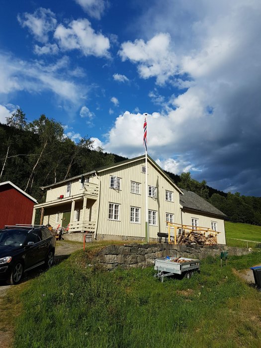 Gammalt tvåvånings församlingshem under renovering, omgivet av grönska med norsk flagga i topp under blå himmel.