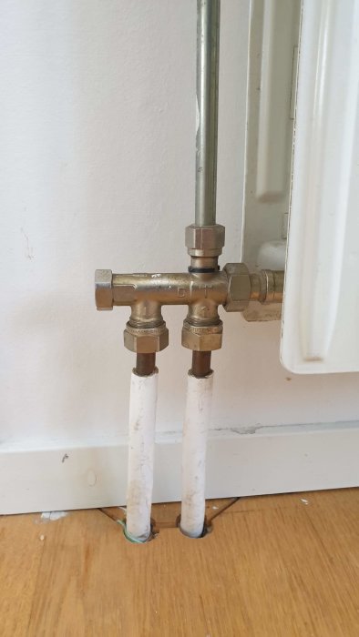 Radiatorkoppling med synliga rör och termostatventil vid vit vägg och radiator.