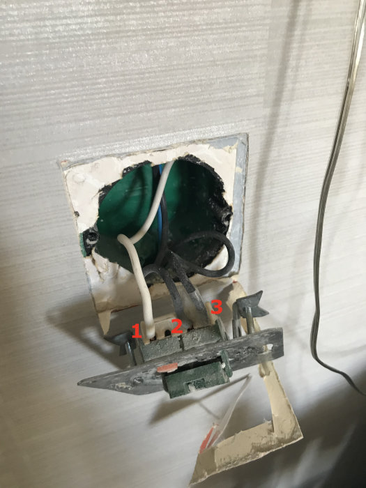 Öppen vägguttag med exponerade kablar och lampknapp, numrerade för diskussion om installation.