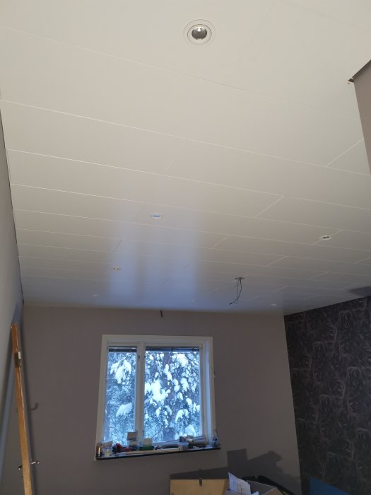 Tak med infällda spotlights och synlig kabeldragning i ett under-renovering-rum med snöutsikt genom fönster.