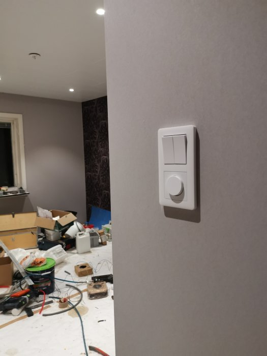 En väggmonterad ljusdimmer från Eljo Exxact i en under renovering rum med byggmaterial och verktyg i bakgrunden.