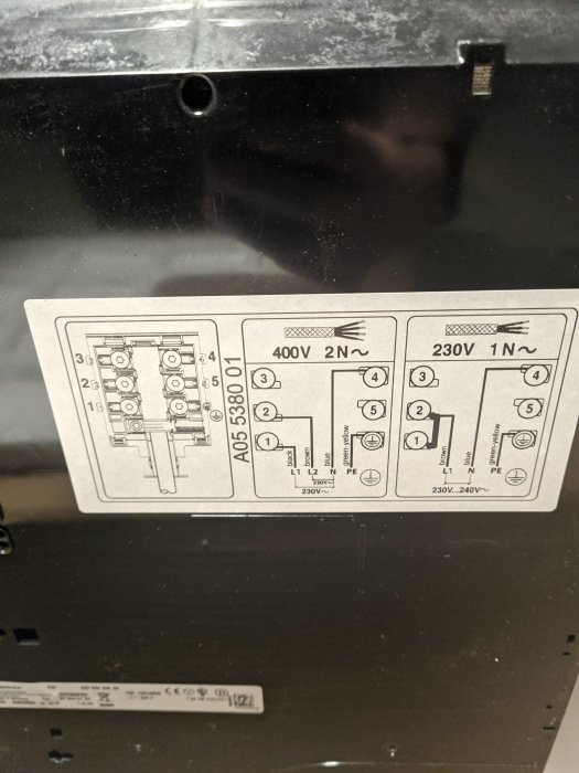 Bild på en anslutningsschemaetikett för en spishäll med instruktioner för olika spänningar och ledarkopplingar.