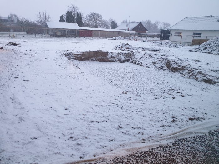 Byggarbetsplats med snötäckt mark och en grävd grop för en pool i väntan på varmare väder.