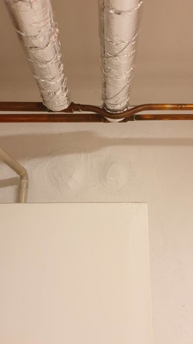 Isolerade rör leder över till en vägg där den nya delen möter den gamla, med synliga tecken på en möjlig anslutningsfel.