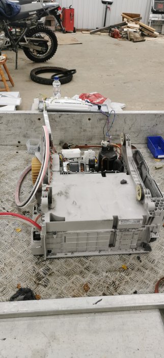 Nedmonterad torktumlare i ett garage med öppna komponenter och verktyg spridda runtomkring.