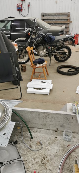 Tumlardelar utspridda i ett garage med en motorcykel, däck och verktyg i bakgrunden.