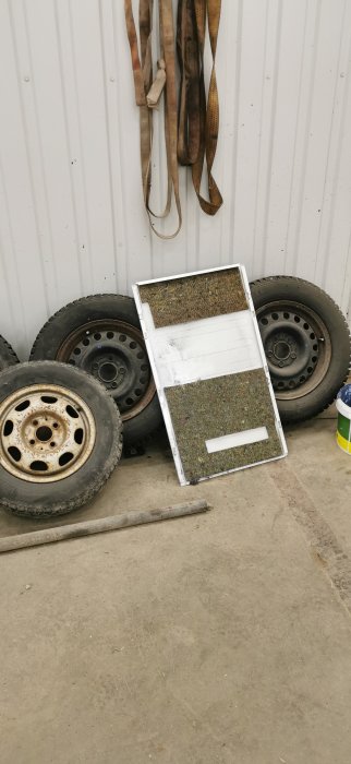 Del av torktumlare med kondensor framför bilhjul och verktyg i ett garage.