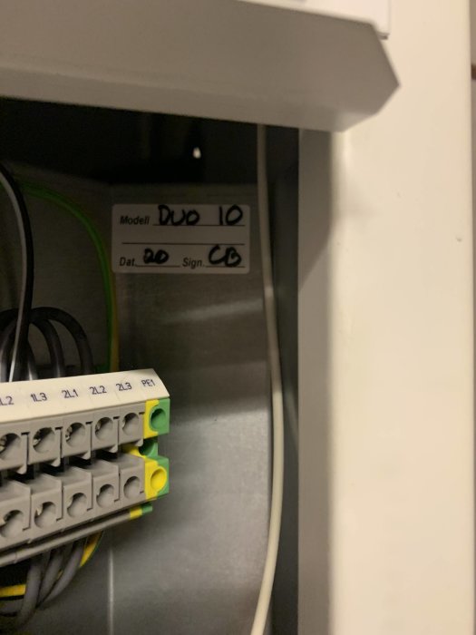 Elskåpets insida med en märkning för 'Modell Duo 10', kablar och säkringsklämmor i fokus.