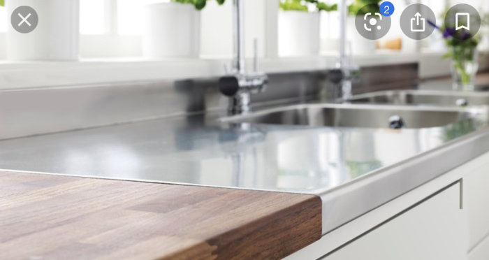 Köksbänk med underlimmad diskho och tjock massiv ekskiva i förgrunden, modern köksdesign.
