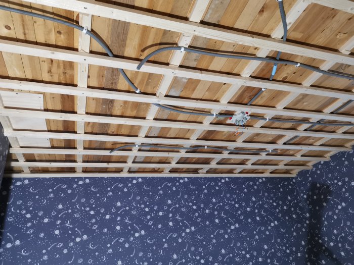 Träreglar i tak med dragen elektrisk kabel och en väggkontakt mot en bakgrund av mönstrad tapet.