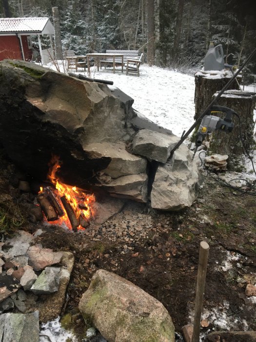 En eld brinner under en klippa i ett vinterlandskap, medan kilar ser ut att användas för att klyva stenen.