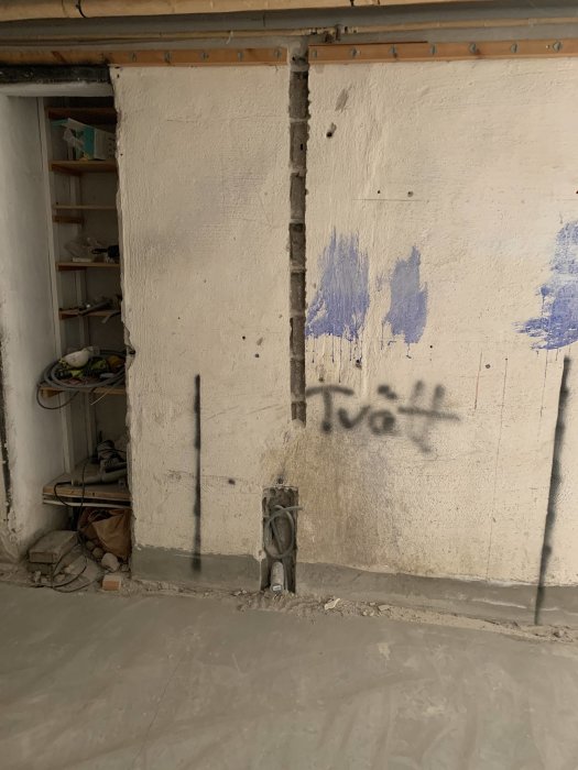 Betongvägg med synliga spår av byggjobb, ledningar och graffiti-texten "Tvätt".