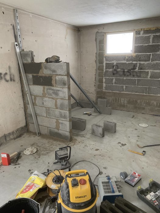 Byggplats invändigt med verktyg, byggmaterial och oavslutad murning.