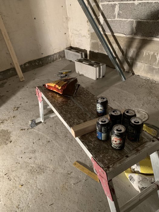 Byggarbetsplats med ölburkar och chipspåse på en hopfällbar arbetsbänk.