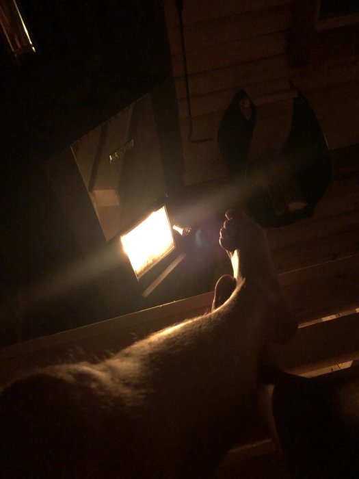 Kvällsbild av en person som vilar sin fot nära en brinnande kamin med svagt ljus.