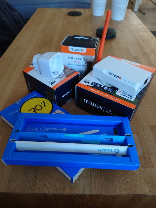Smart home uppgraderingskit inklusive Tellstick Net, plug-in switch och Sensative Strips Drip fuktsensorer på ett bord.
