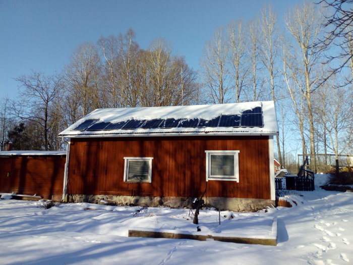 Solceller på ett snötäckt hustak med delvis borttagen snö under en klar himmel.