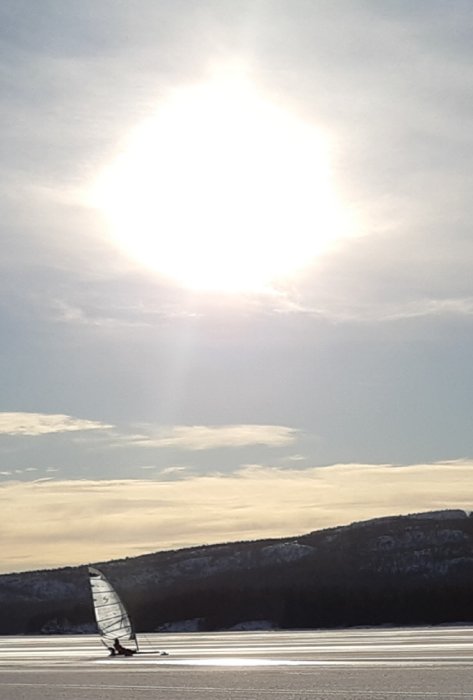 Isbana med en person som åker isskridskor under en klar himmel med starkt solljus.