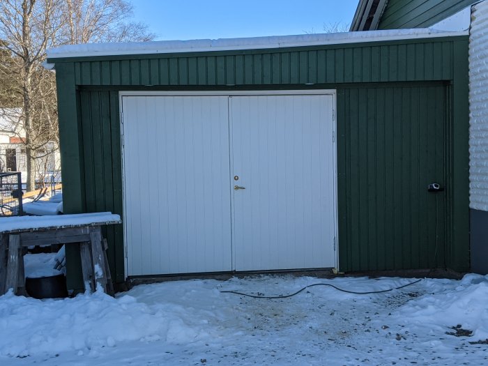 Vit garageport på grönmålat garage med snö runtomkring.