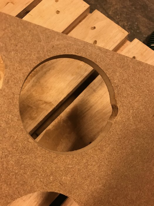 Nyligen fräst rund öppning i en MDF-skiva, visar tecken på skador där den inre cirkeln lossnat.