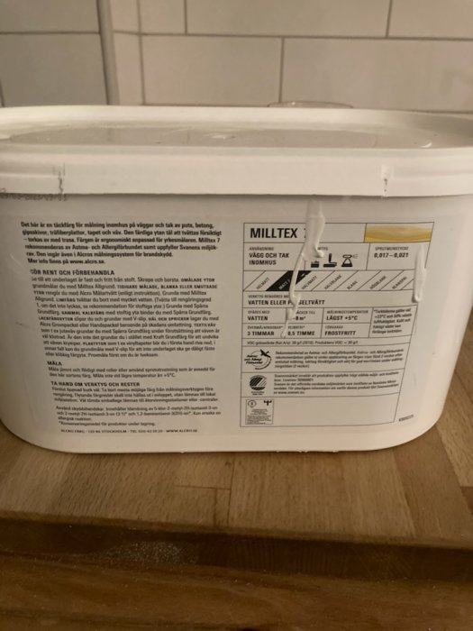 Hink med färg och instruktioner för användning i köksmiljö på köksbänk mot kakelvägg.