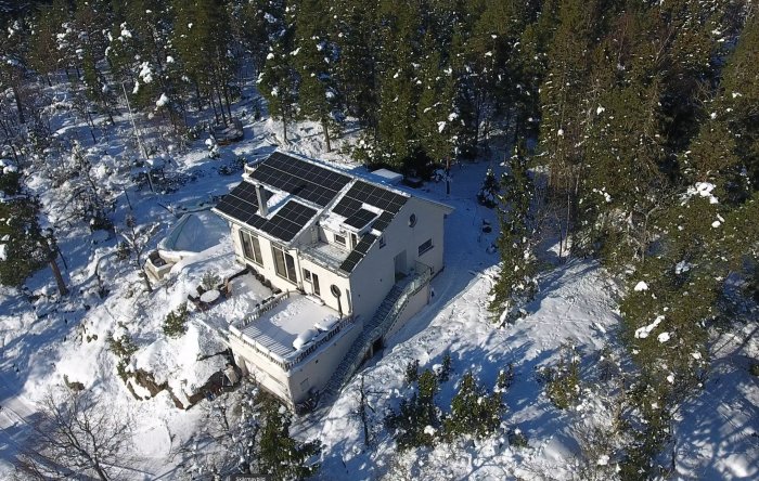 Ett hus omgivet av snö med rensade solpaneler på taket, sedd från ovan.