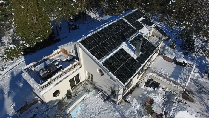 Flygfoto av ett hus i vinterskrud med snöfria solpaneler på taket.