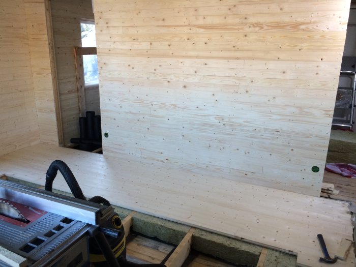 Inredning av byggprojekt med träväggar och isolering synlig på golvet, verktyg i förgrunden.