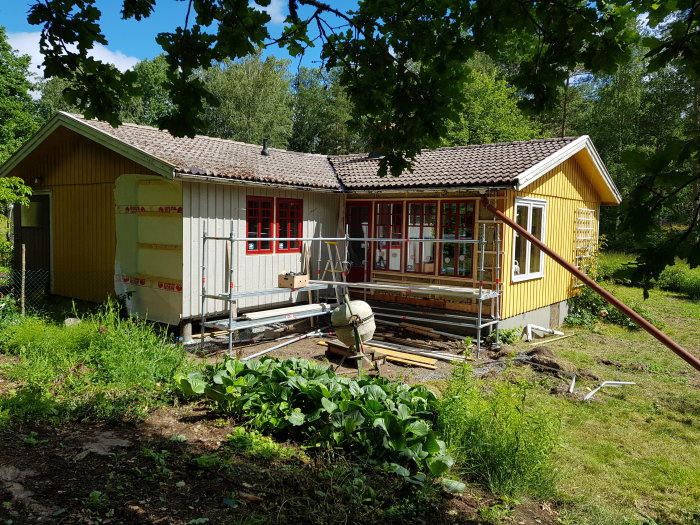 Renovering av gult hus där en person hjälper till att installera nya röda fönster och en altandörr.