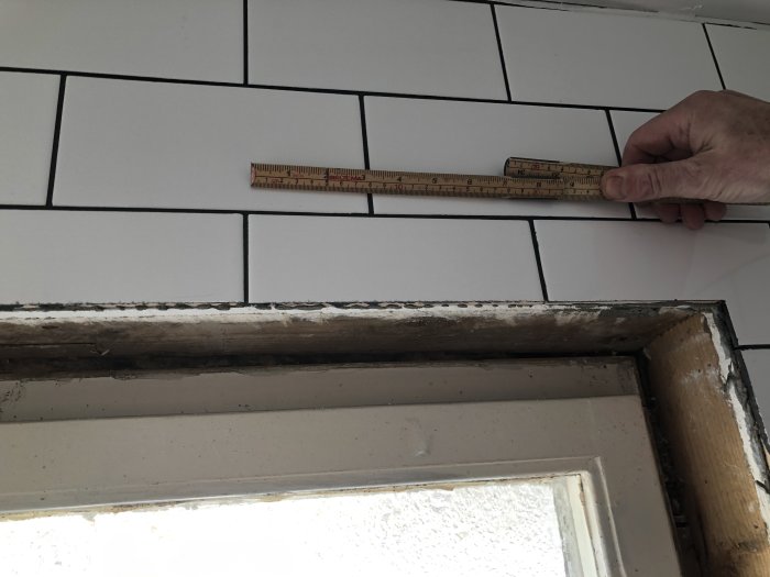 En hand håller en linjal mot kakelplattor för att mäta ojämnhet vid en tröskel.