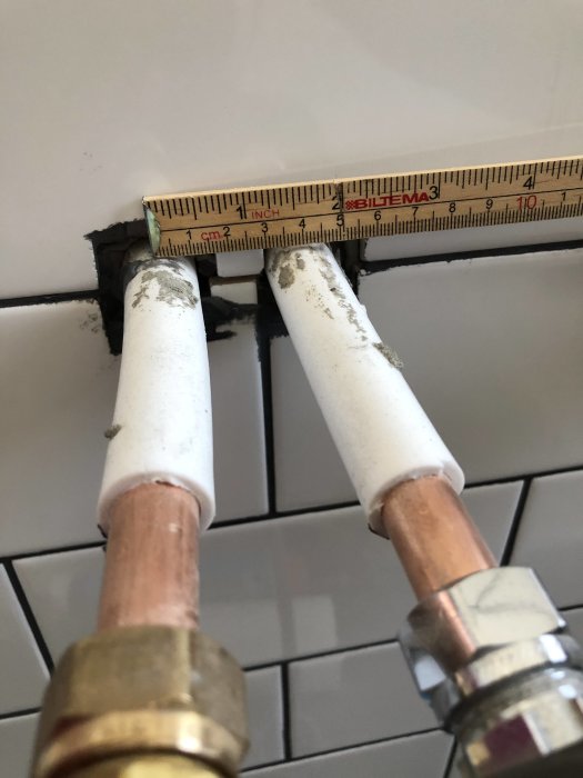 Måttband visar avstånd vid väggen mellan två kopparrör som sticker fram ur kakel.