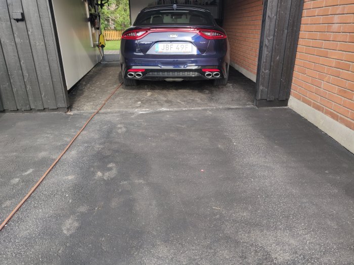 Nybelagd asfalterad uppfart med en blå bil parkerad nära garageporten.