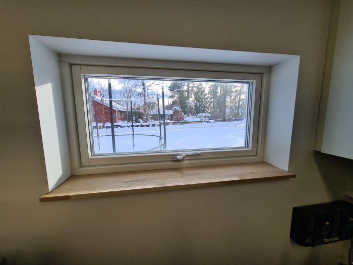 Nyinstallerad fönsterbräda i garage med utsikt över snötäckt trädgård och röd byggnad.