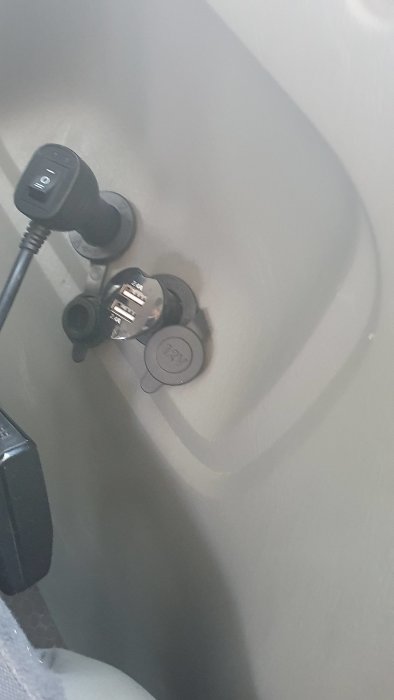 Monterat biluttag med dubbla USB-portar och 12V-kontakt dolt längs fordonets interiör.