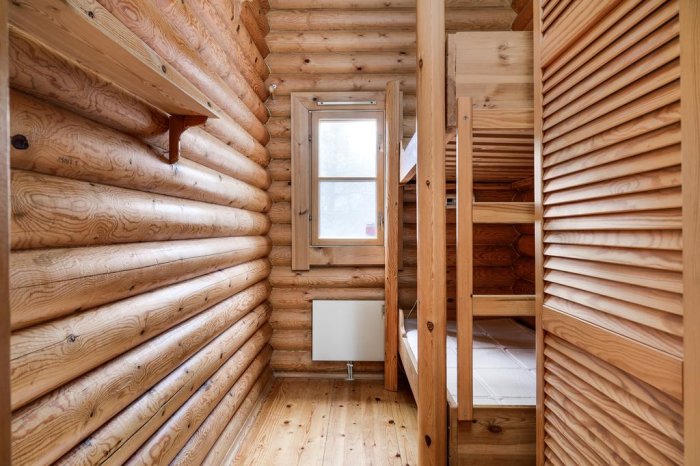 Interiör av en sommarstuga med obehandlade timmerväggar, trägolv och en inbyggd våningssäng.