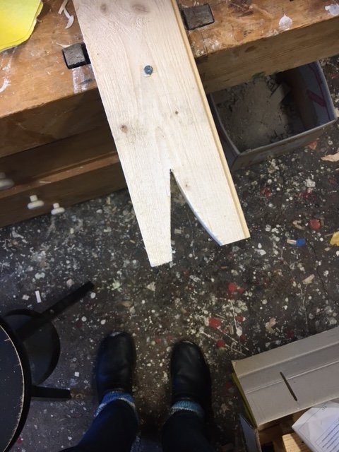 Ett hemmagjort sågstöd på en arbetsbänk klart med två borrade hål, med rörigt verkstadsgolv i bakgrunden.