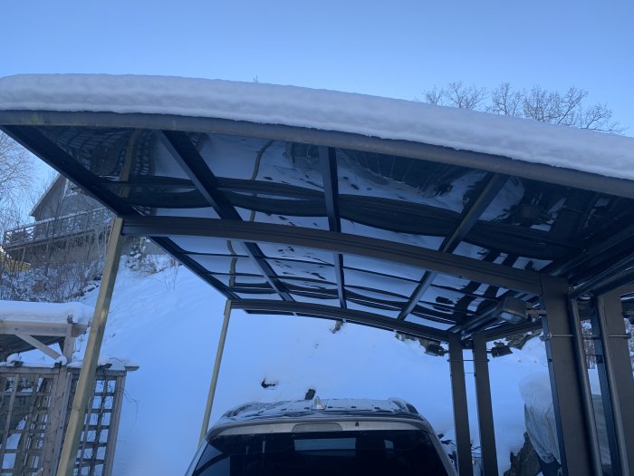 Carport med tung snölast på taket och bil parkerad under.