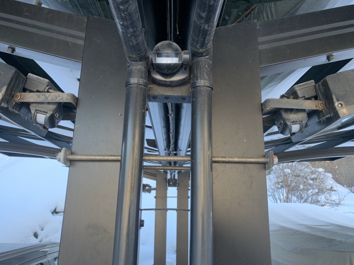 Underifrån bild på förstärkta takbalkar i en carport med snö ute.