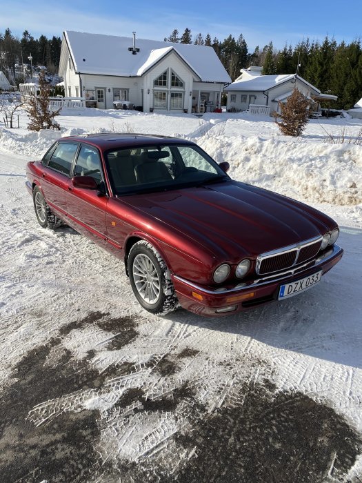 Röd Jaguar-parkering framför hus i vintersnö med klarblå himmel.