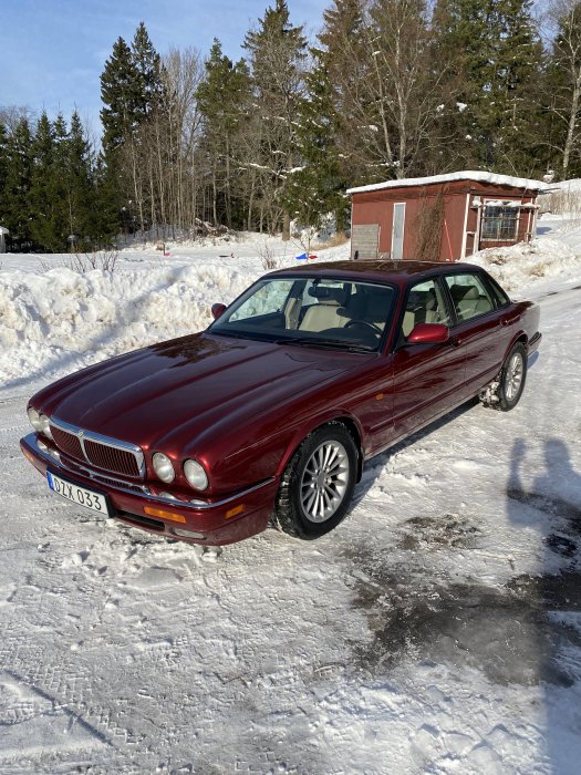 Röd Jaguar bil parkerad på en snötäckt väg med skog i bakgrunden och en röd stuga.