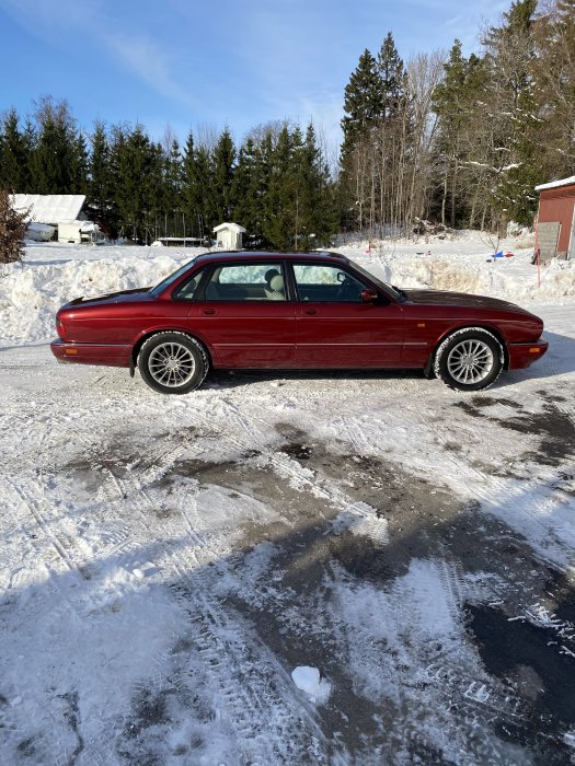 Röd Jaguar-bil parkerad på en snötäckt väg med träd i bakgrunden.