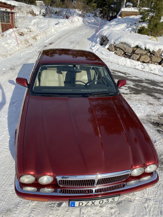 Rodd färgad Jaguar parkerad på en snöig uppfart under solljus.