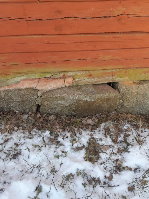 Skadad syll och sten som tryckts upp av tjäle vid en husgrund med snötäckt mark runtomkring.