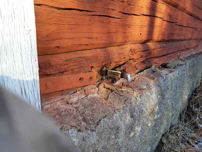 En del av en syll med tecken på skador och en tidigare lagning, med en grundsten synlig och en ficklampa vilande mot den.